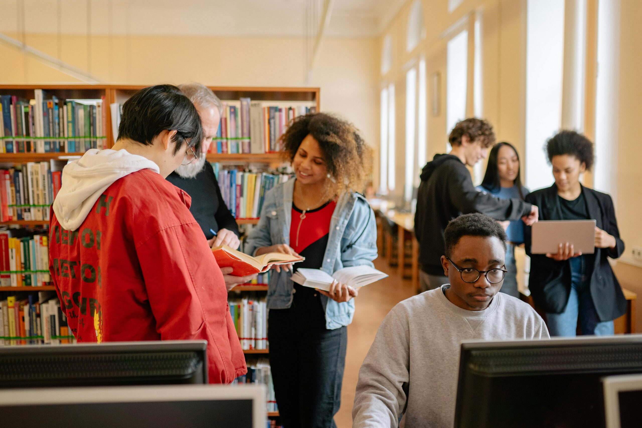 Two groups browsing books in a library, while another person works at a computer.