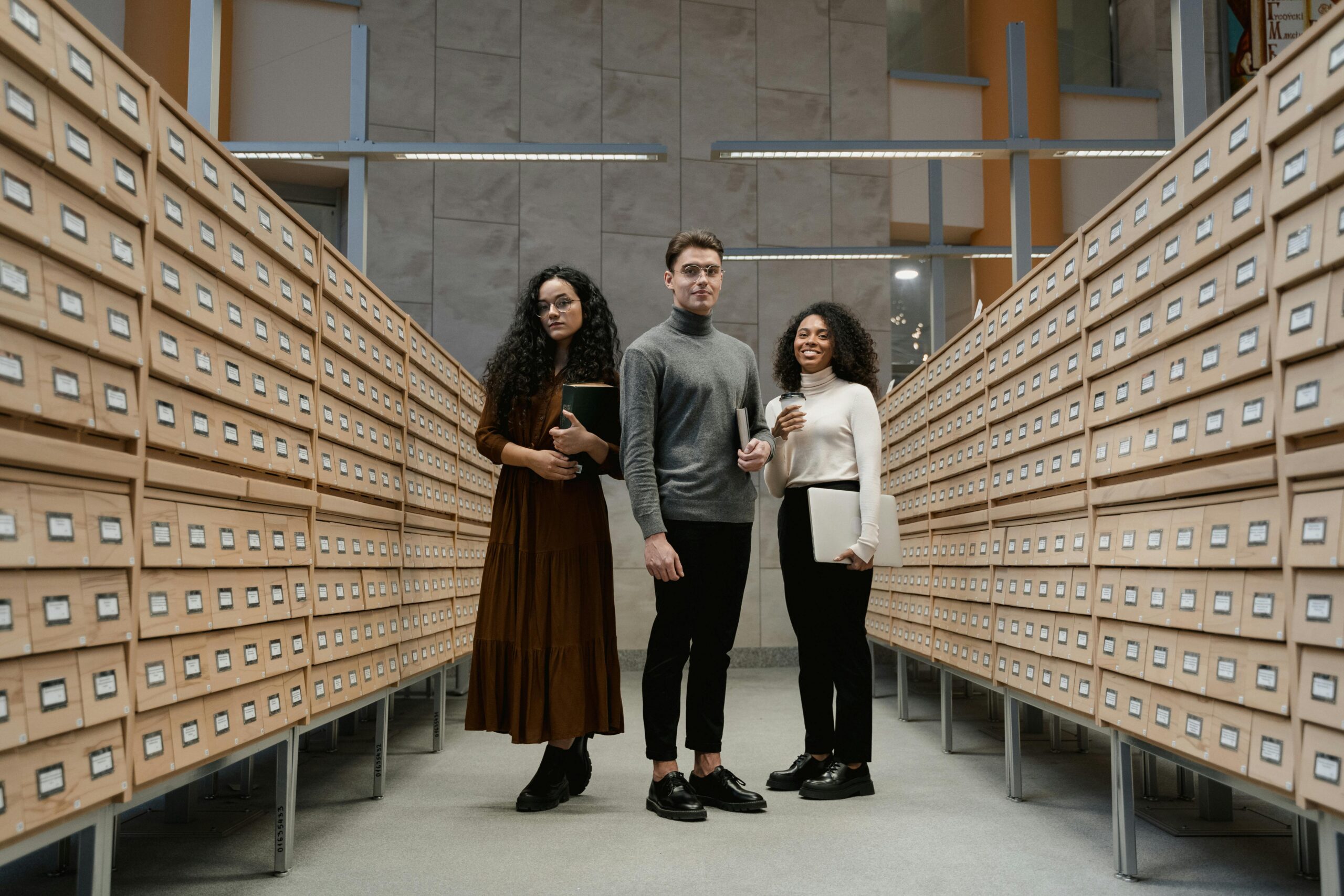 Two woman and one man standing in an aisle of small drawers.